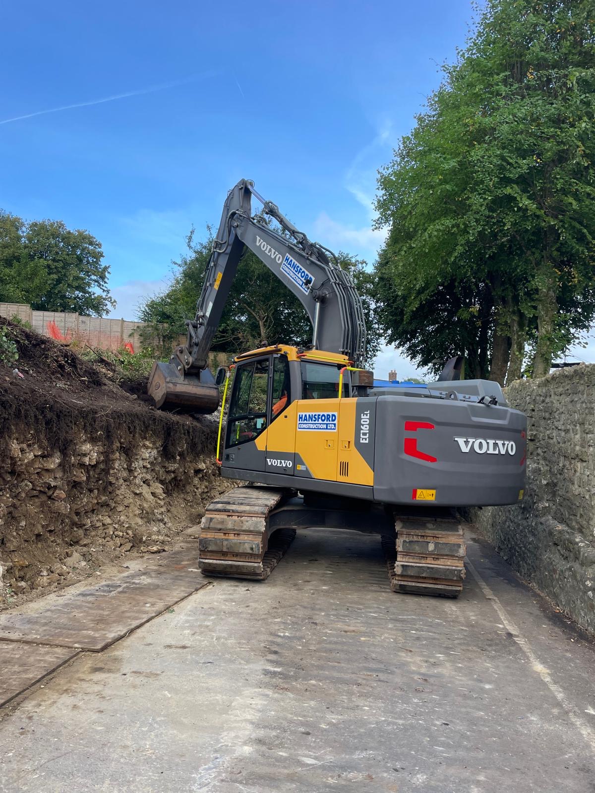 Excavator removing the old retaining wall during groundworks.